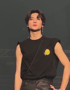 a woman with black hair wearing a black shirt and silver earrings on her head, standing in front of a dark background