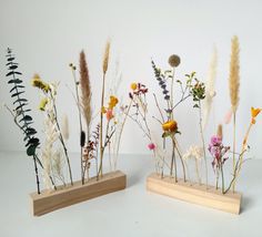 three wooden vases filled with different types of wildflowers on top of a white surface