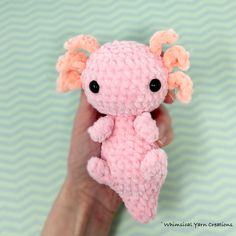 a hand holding a small pink crocheted stuffed animal with horns on it's head