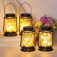 three mason jars with fairy lights in them sitting on a table next to some flowers