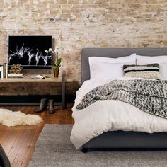 a bedroom with exposed brick walls and a bed in the middle, next to a tv