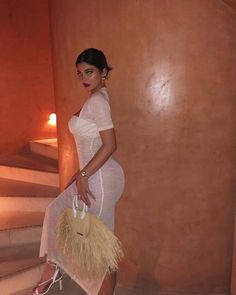 a woman in a white dress is holding a straw bag and posing for the camera