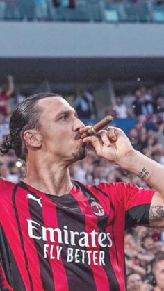 a man in a red and black shirt eating a hot dog at a soccer game