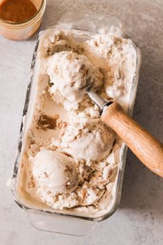 two scoops of ice cream in a glass container with a wooden spoon next to it