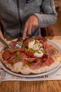 a person cutting into a pizza on top of a white plate