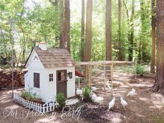 a small white house in the middle of a forest with chickens and trees around it