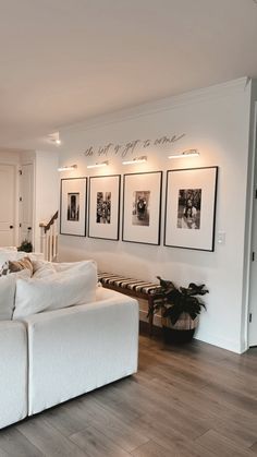 a living room with white furniture and pictures on the wall