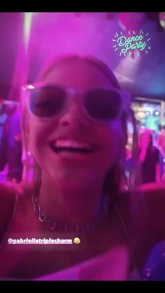 a woman wearing sunglasses and smiling in front of a crowd at a party with other people