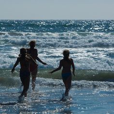 three people are walking in the water at the beach