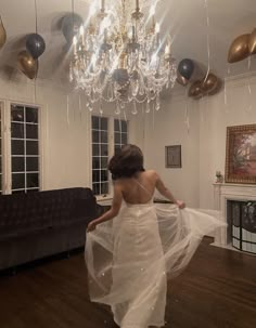 a woman in a white dress is walking through a room with balloons hanging from the ceiling