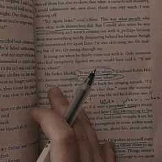 a hand is holding a pen and writing on an open book with the pages turned down