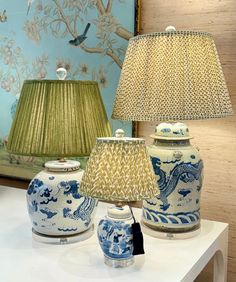 three blue and white vases on a table with a lamp next to them in front of a painting