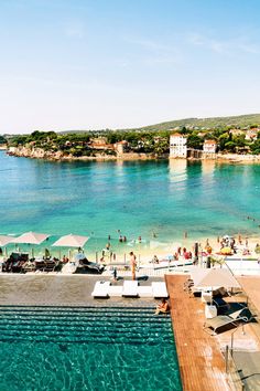 the beach is crowded with people and umbrellas in clear blue water, surrounded by green hills