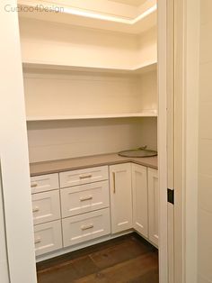 an empty kitchen with white cupboards and counters in the corner, looking into the pantry