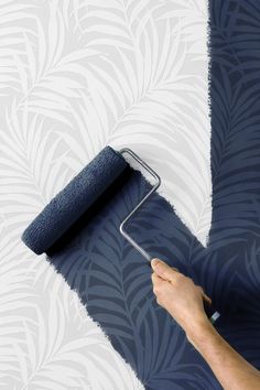 a person painting a wall with a blue paint roller and palm leaf pattern on it