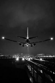 an airplane is flying low over the city at night with its lights on and it's landing gear down