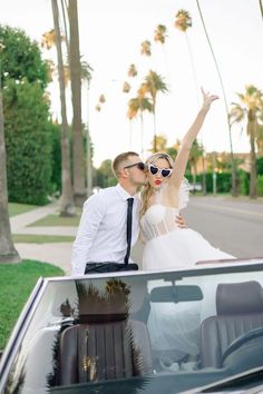 a man and woman standing next to each other in front of a car with palm trees