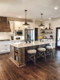 a kitchen island with stools in the middle and lights hanging from it's ceiling