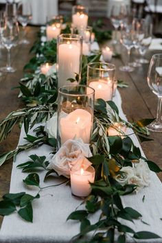 a long table with candles and greenery on it, surrounded by wineglasses