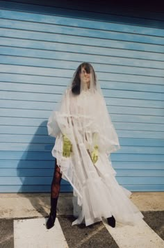 a woman wearing a white dress and veil standing in front of a blue wall with her hands on her hips