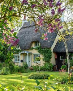 a thatched roof house with pink flowers in the front yard