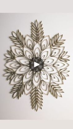 a metal snowflake hanging on the wall in front of a white wall with leaves