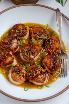 a white plate topped with scallops covered in sauce and garnished with green onions