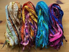 four different colors of scarves laid out on a wooden surface with string attached to them