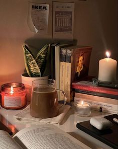 an open book on a table next to a lit candle and some books with candles