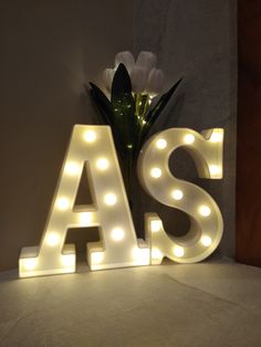 the letters as are lit up with lights and flowers in front of a white wall