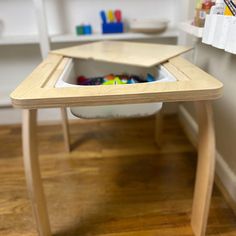 a wooden table with a hole in the center filled with colored pencils and crayons