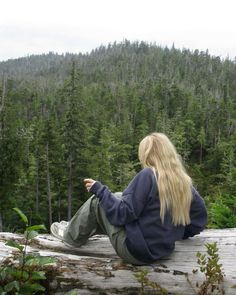 a woman sitting on top of a log in front of a forest filled with trees