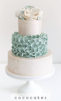 a three tiered cake with blue and white frosting flowers on the top layer