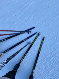 four pairs of skis laying in the snow with one person's feet propped up