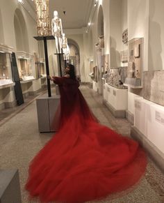 a woman in a long red dress is looking at some art on the walls and floor