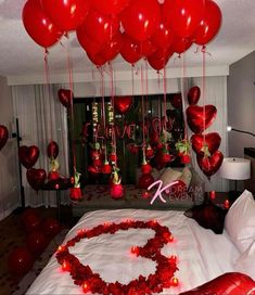 a bed topped with lots of red heart shaped balloons