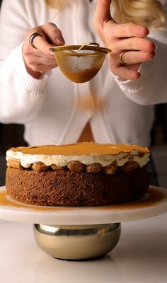 a woman is pouring something into a cake on a plate with a bowl in front of her