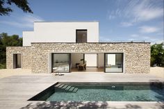 a house with a pool in front of it and a stone wall on the side