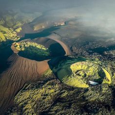 an aerial view of some green hills and rivers in the distance, with clouds overhead