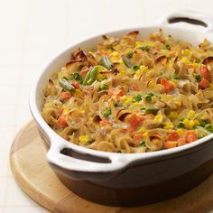 a casserole dish with noodles and vegetables in it on a wooden board next to a knife