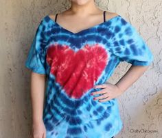 a woman standing in front of a wall wearing a tie dye shirt with a heart on it