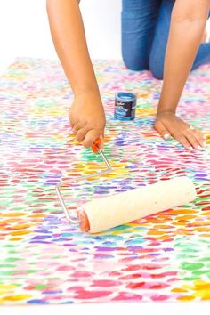 two children are painting on a colorful table cloth with paint rollers in front of them