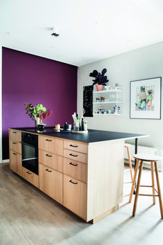 a kitchen with purple walls and black counter tops, two stools in front of the island