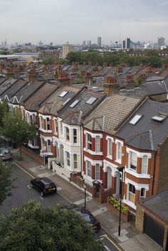 a row of houses with cars parked on the street in front of them and tall buildings