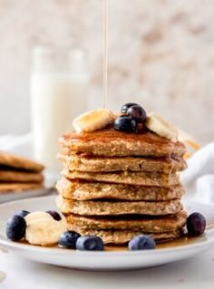 a stack of pancakes with blueberries, bananas and syrup being drizzled over them