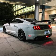 the rear end of a white mustang parked in front of a large building at night