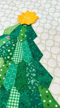 a quilted christmas tree made with green and yellow fabrics on a white tablecloth