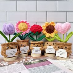 four crocheted pots with flowers in them on a table next to a newspaper