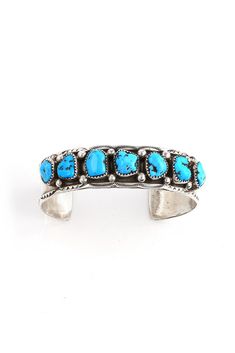 This Marie Thompson Kingman Turquoise Row Cuff is the perfect bracelet for a large wrist. Navajo silversmith, MarieThompson, has created this traditional row bracelet with 7 genuine Kingman Turquoise stones. She added handmade sterling silver beads between each stone and hand-stamped Navajo designs along the edge of the bracelet. The sterling silver was oxidized to bring out the details and give this cuff a vintage look. Hallmarked "MT" and stamped "Sterling". Fits 7.25" wrist, adjustable Navajo Designs, Silver Eagles, Turquoise Stones, Kingman Turquoise, Handmade Sterling Silver, Sterling Silver Bead, Turquoise Stone, The Edge, Vintage Look