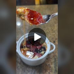 a spoon full of sauce being drizzled over food in a small bowl